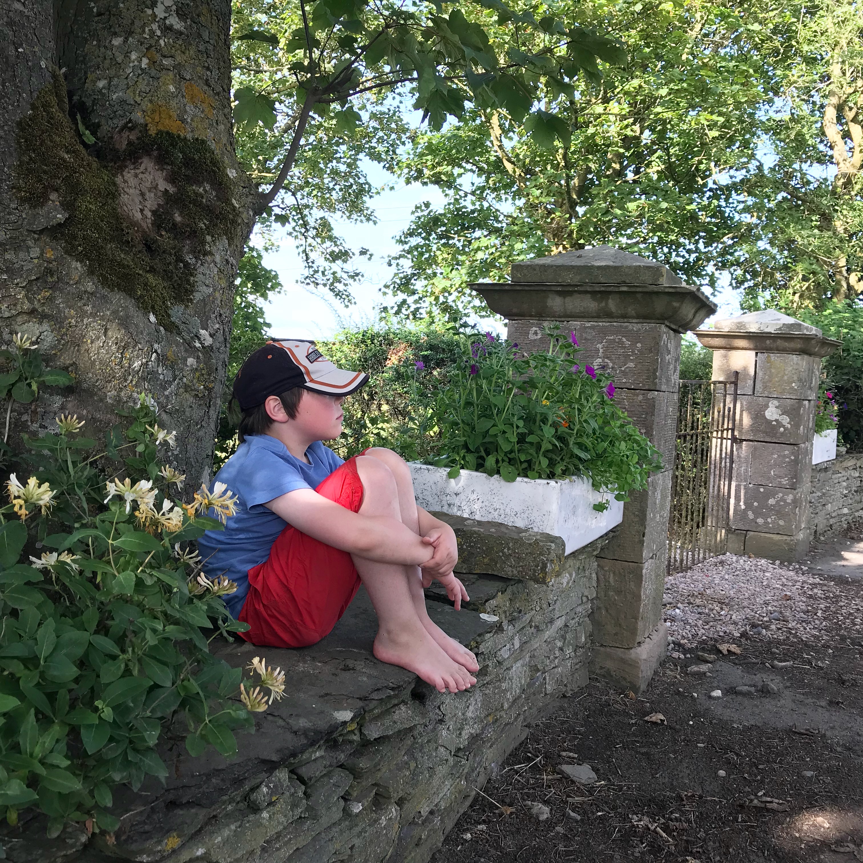 Picture of boy sitting on wall in summer clothes and bare feet
