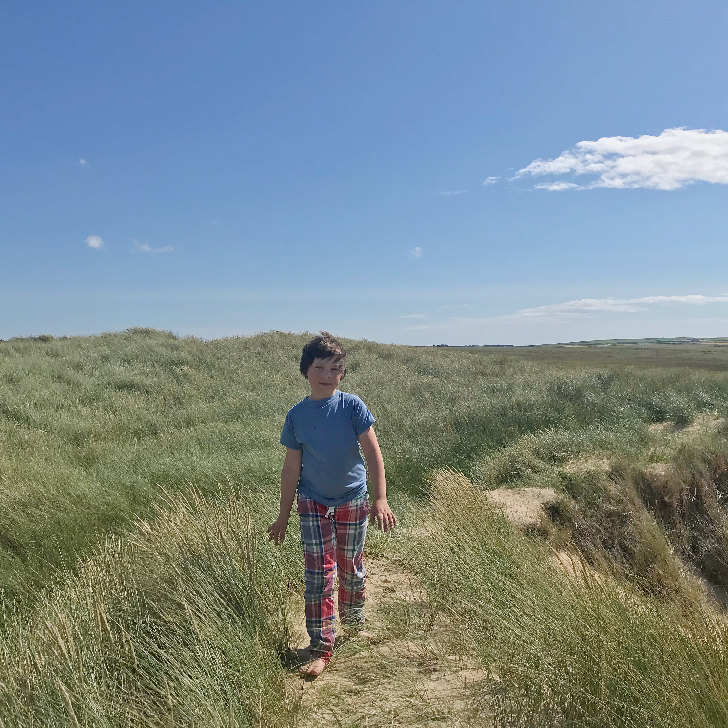Photo of boy walking along sand dunes
