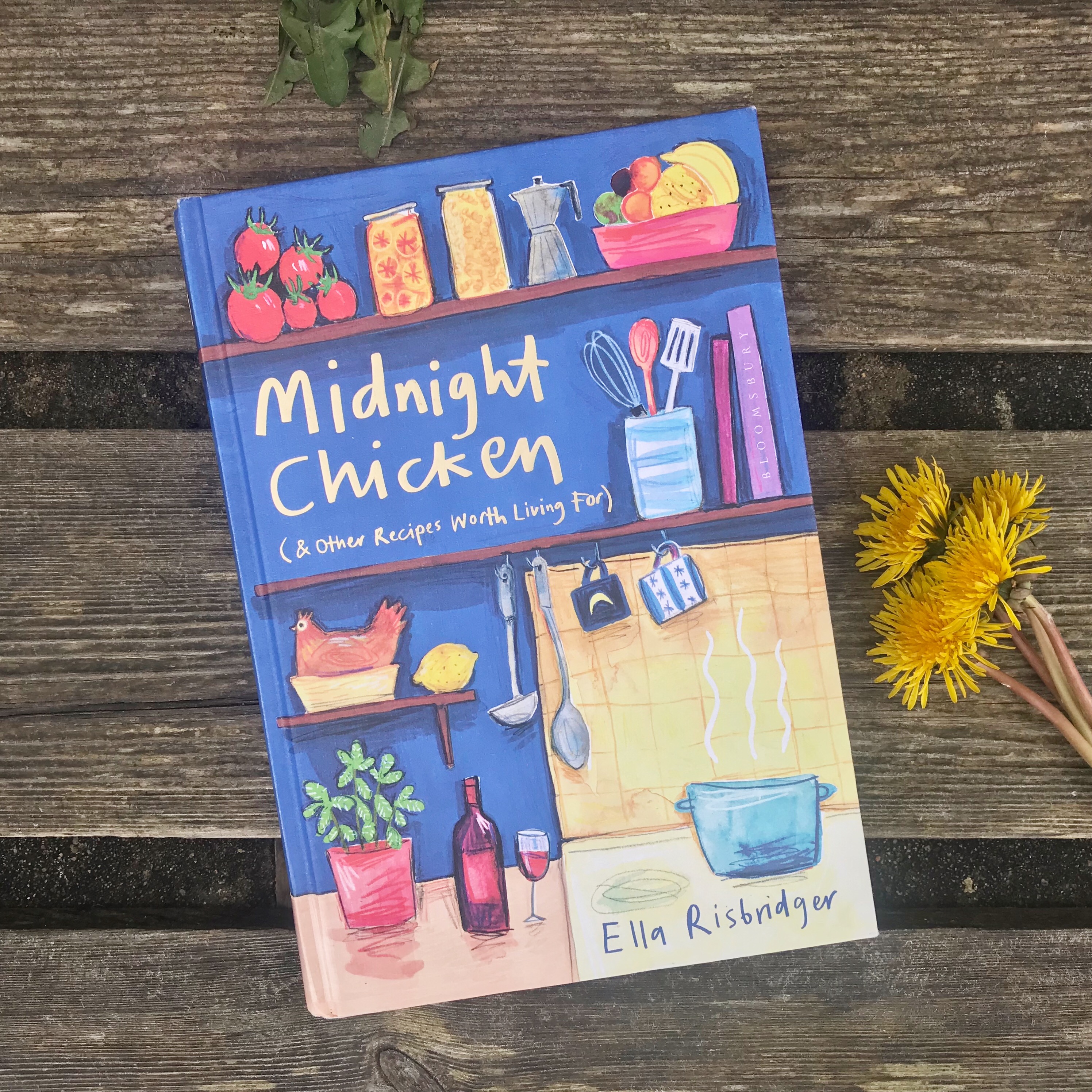 Picture of 'Midnight Chicken' cookery book on bench next to dandelions