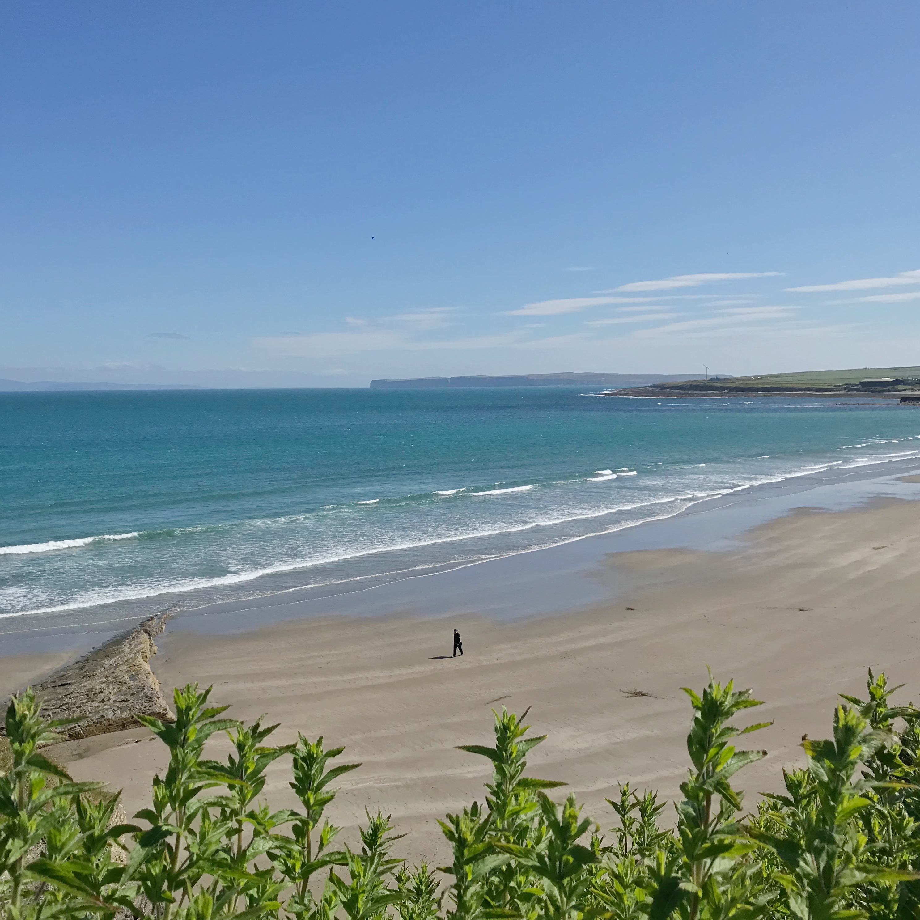 View of person walking along Thurso beach on sunny day