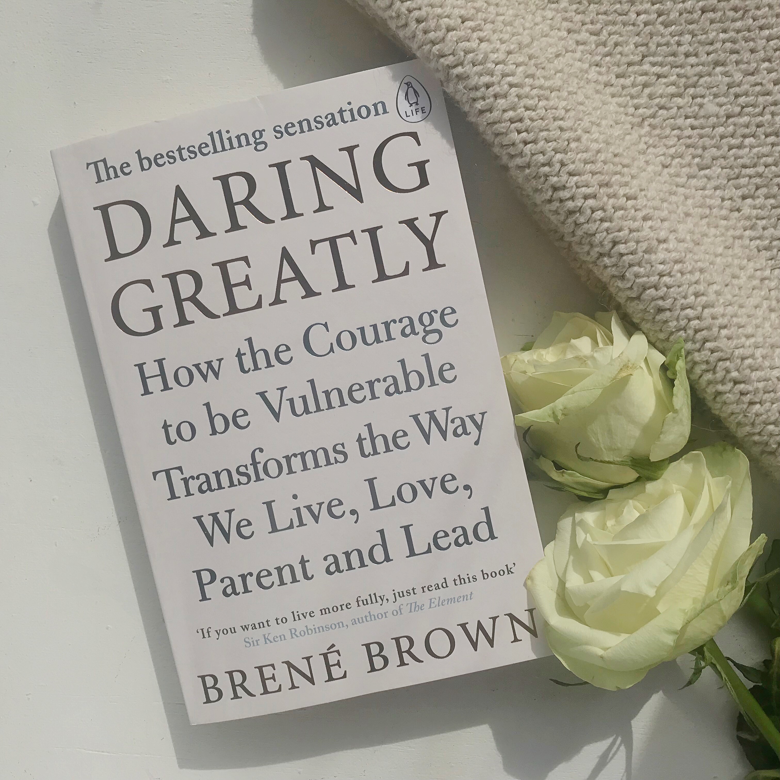 Flatlay picture of Daring Greatly by Brene Brown with flowers