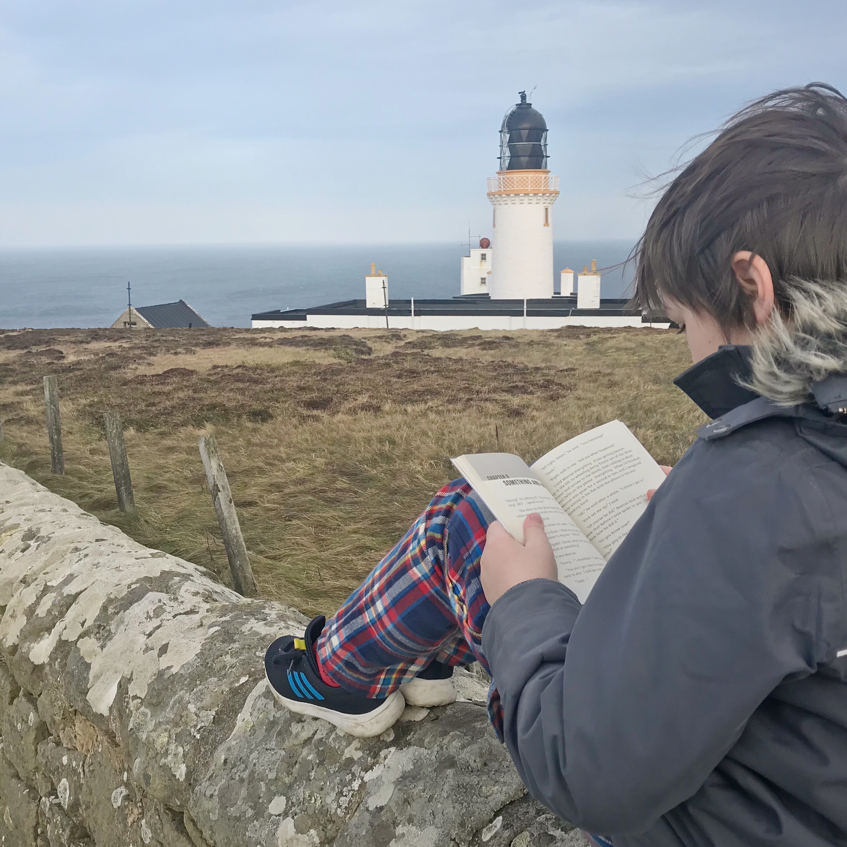 Boy reading next to lighthouse at Dunnet Head, Caithness