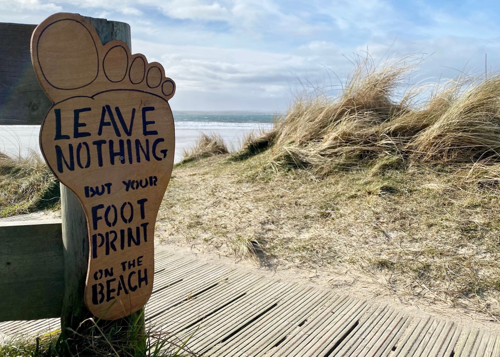 Picture of sign on beach saying ‘leave nothing but footprints.’